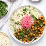 A plate with white rice, chickpea and spinach curry, pickled onions, lime wedge, and cilantro, surrounded by bowls of rice, chopped cilantro, and pink onions. Text: Chana Saag Easy Instant Pot Recipe.