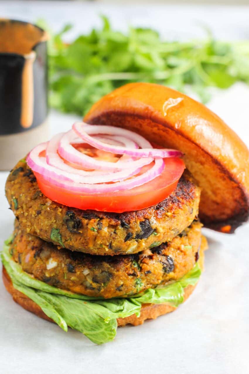 2 burger patties stacked on a bun and topped with tomato and onion 
