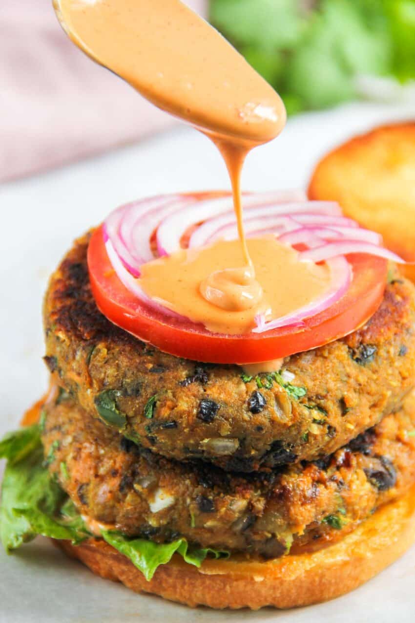 adding sriracha mayo sauce over sweet potato and black bean burger