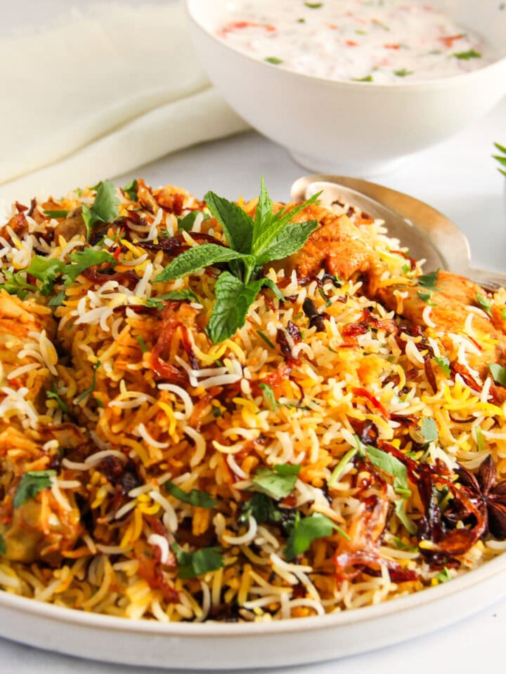 chicken biryani in a serving platter with raita bowl on the side,
