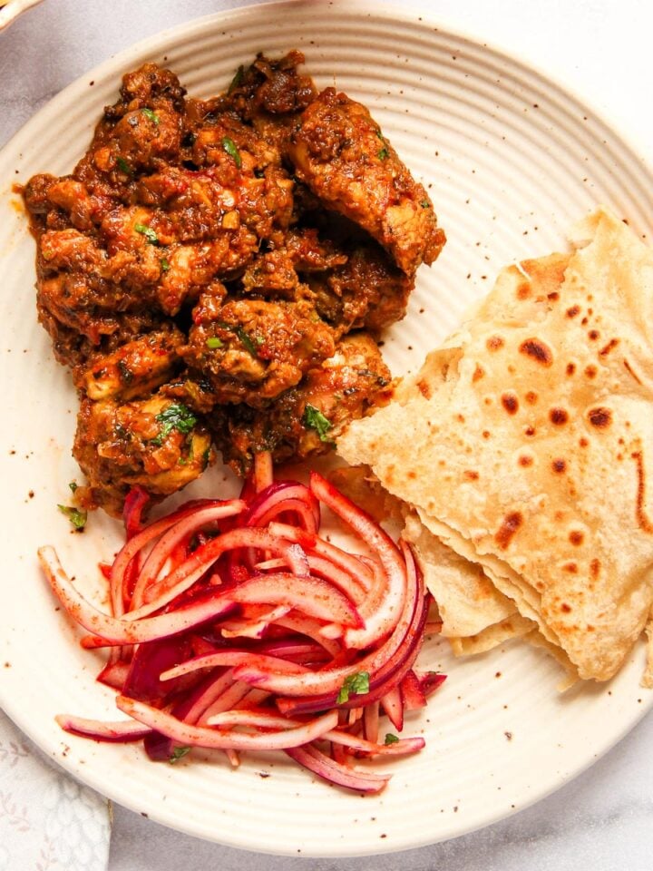 A plate with chicken sukka, sliced red onions , and roti.