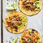 3 Chicken Tinga Tacos on parchment paper with lime wedges