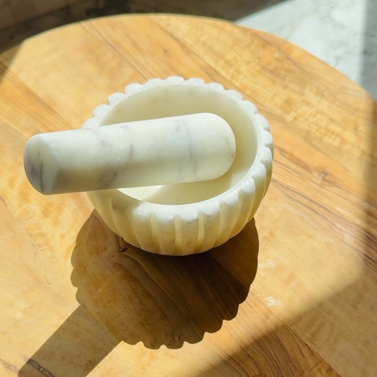 White marble mortar and pestle resting on a wooden surface.