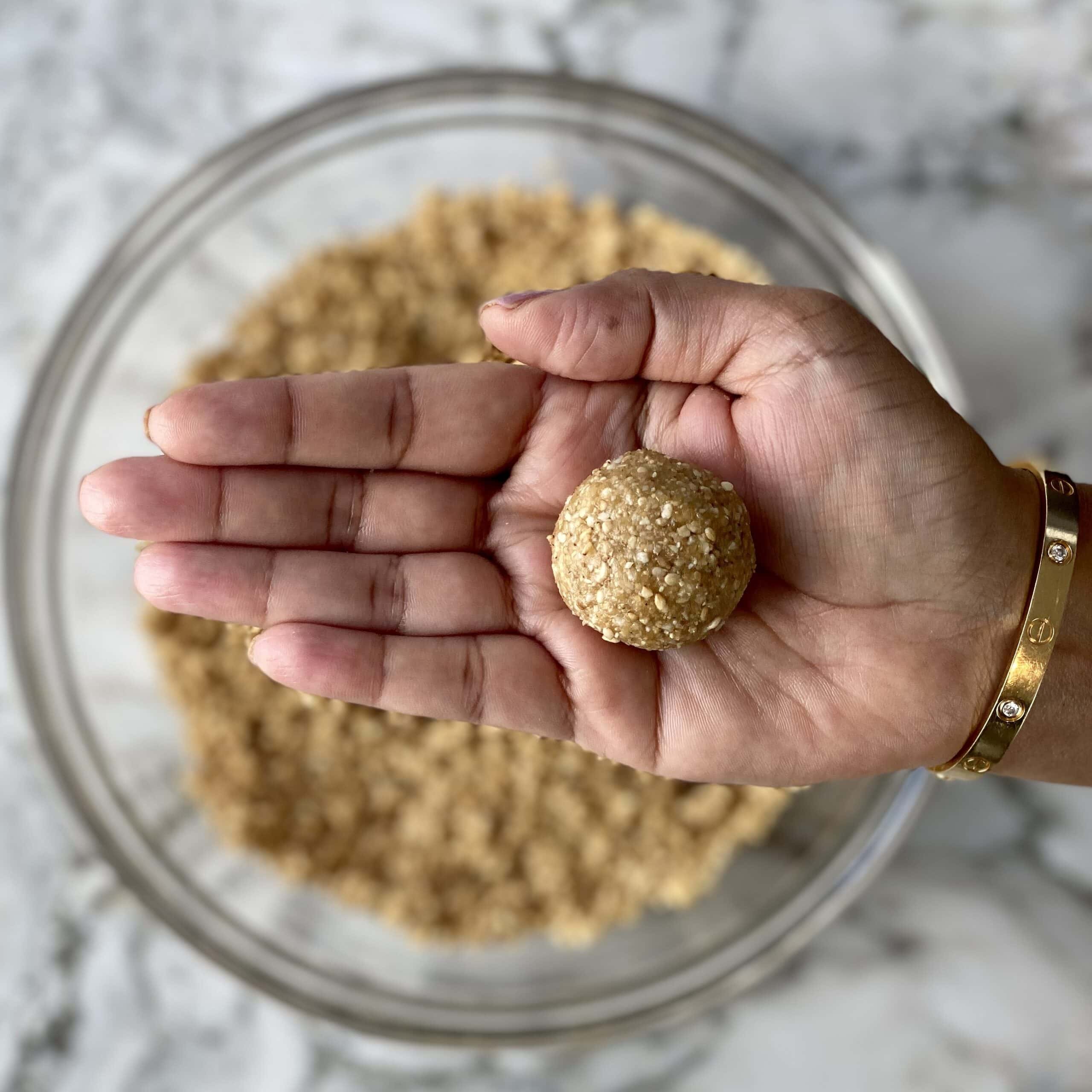 showing a rolled til gud laddu in hand.