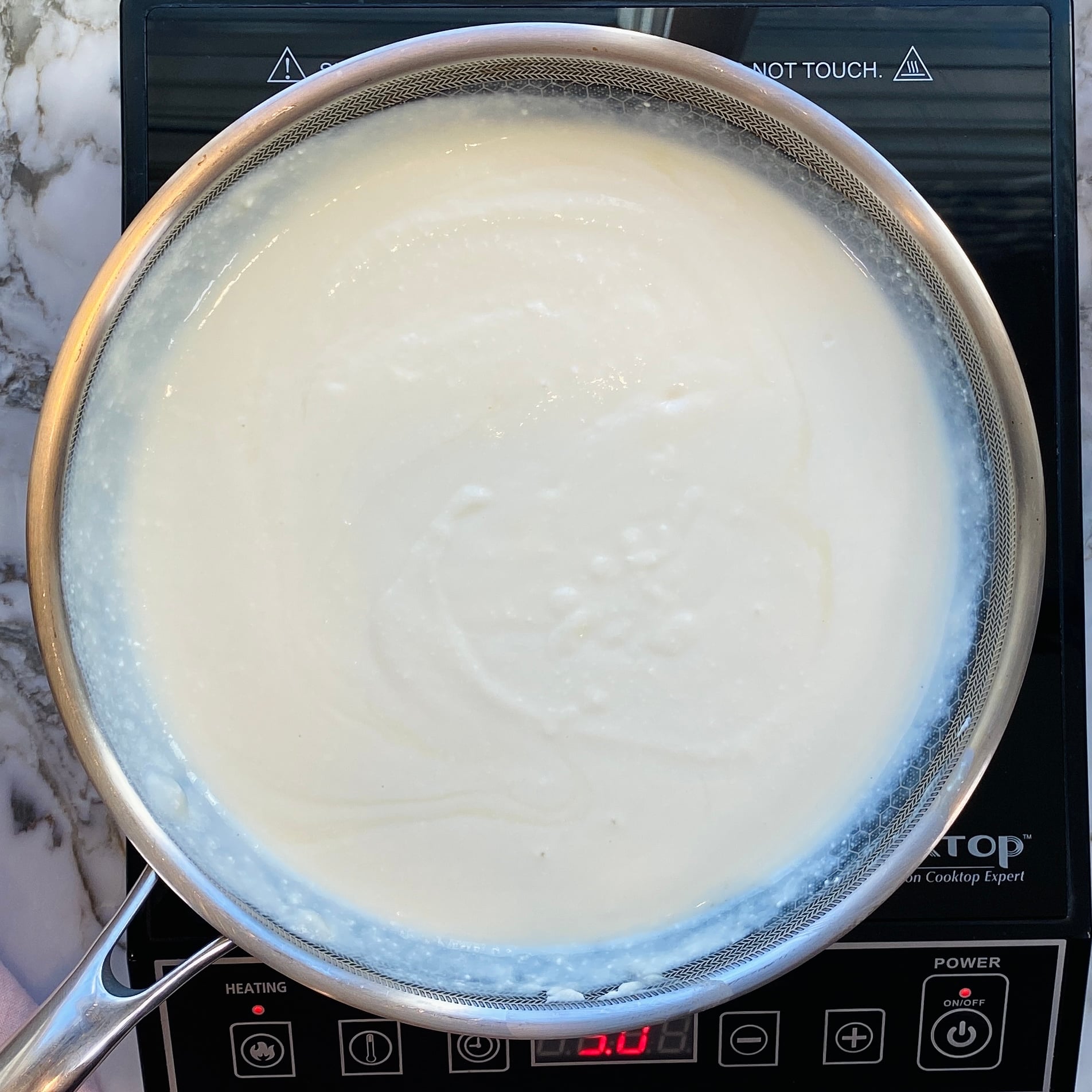 A saucepan filled with white liquid, possibly milk, is heating on an electric stovetop with digital controls.
