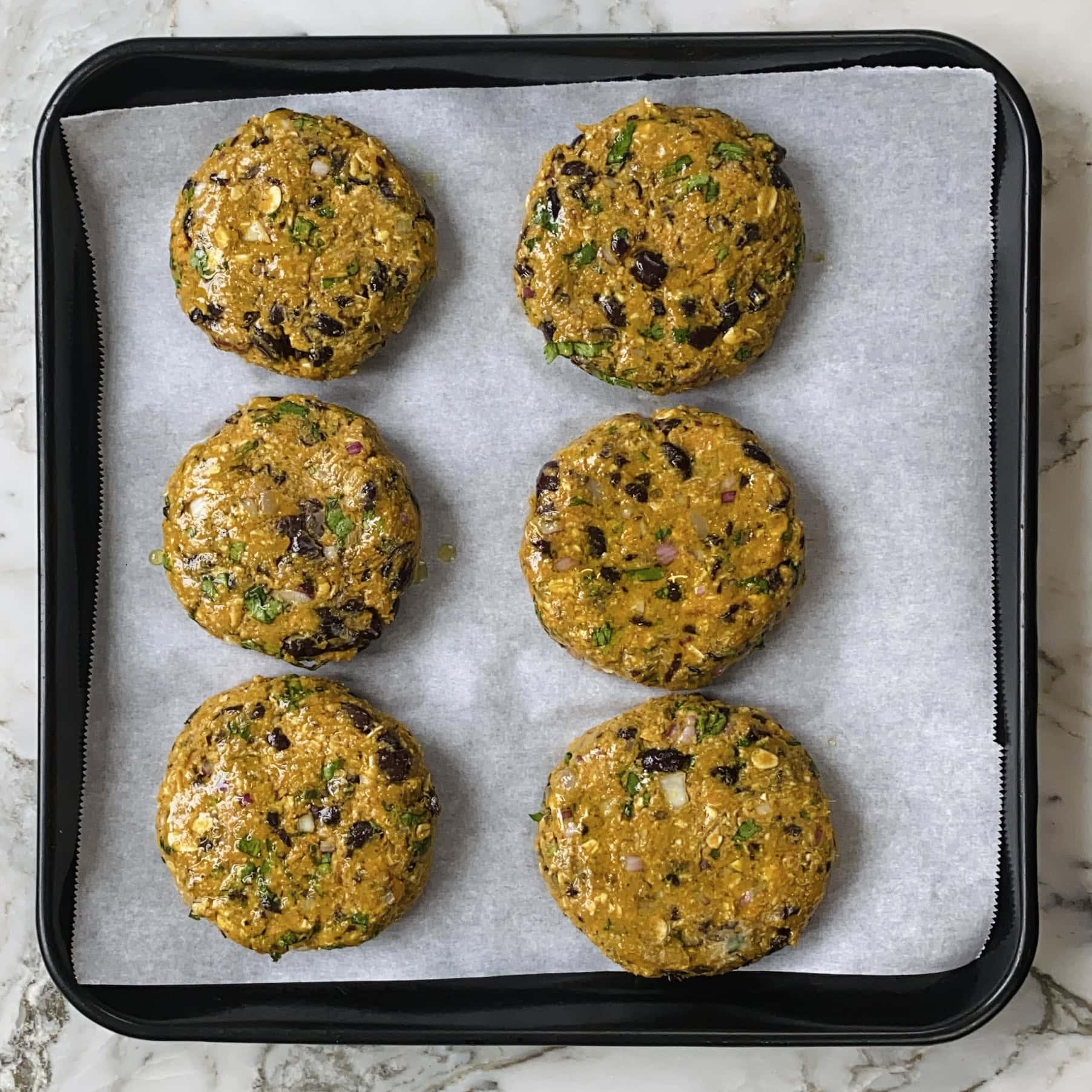Six uncooked veggie burger patties are arranged in two rows on a parchment-lined baking tray.