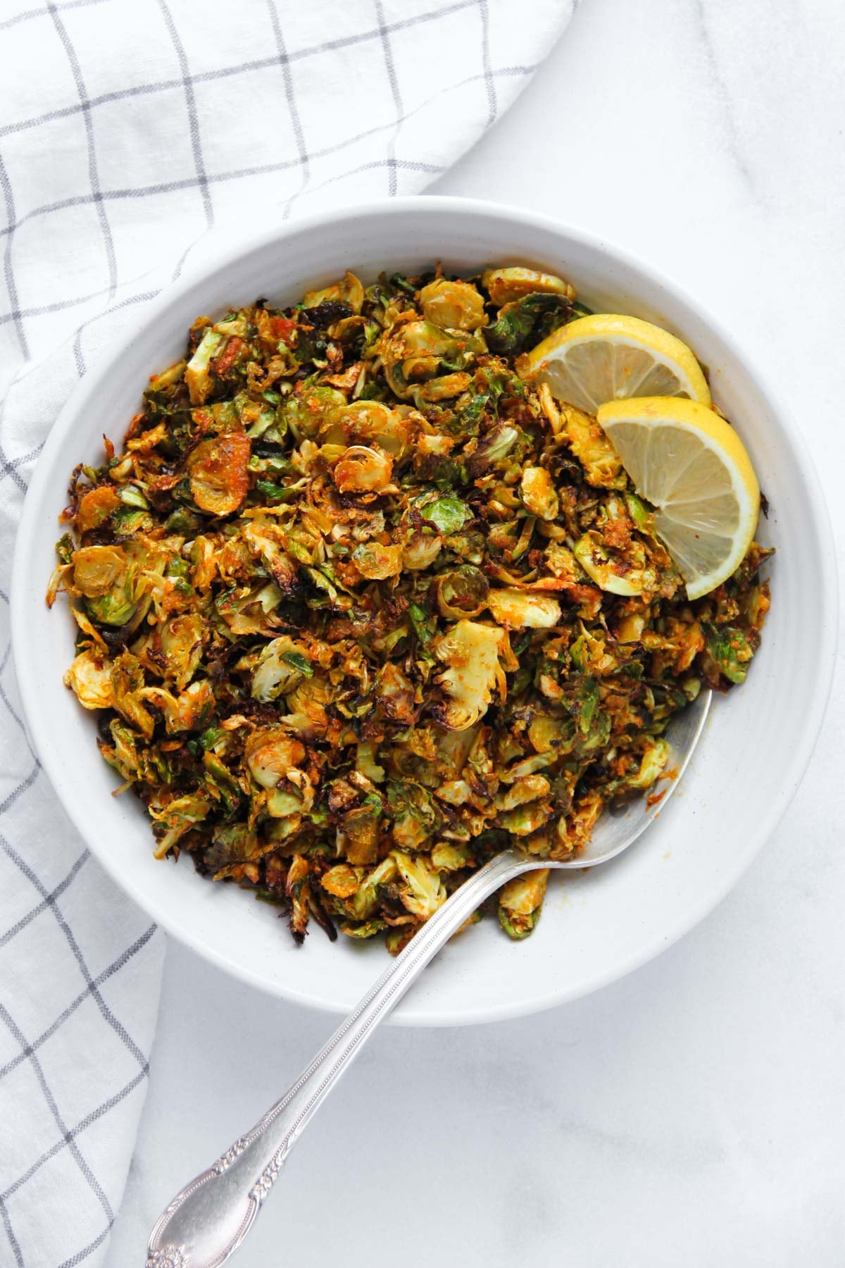 Crispy roasted brussels sprouts in a white bowl with lemon wedges