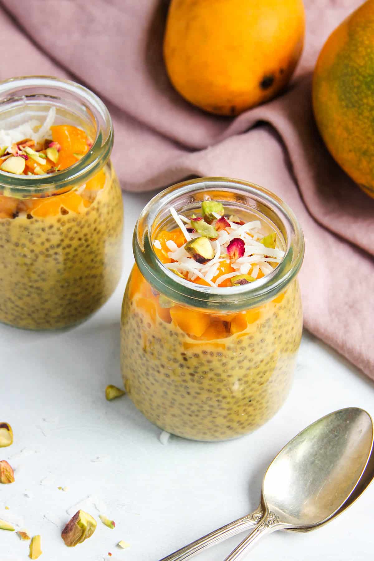 Mango chia pudding in a two glass jars garnished with diced mango, coconut and pistachios