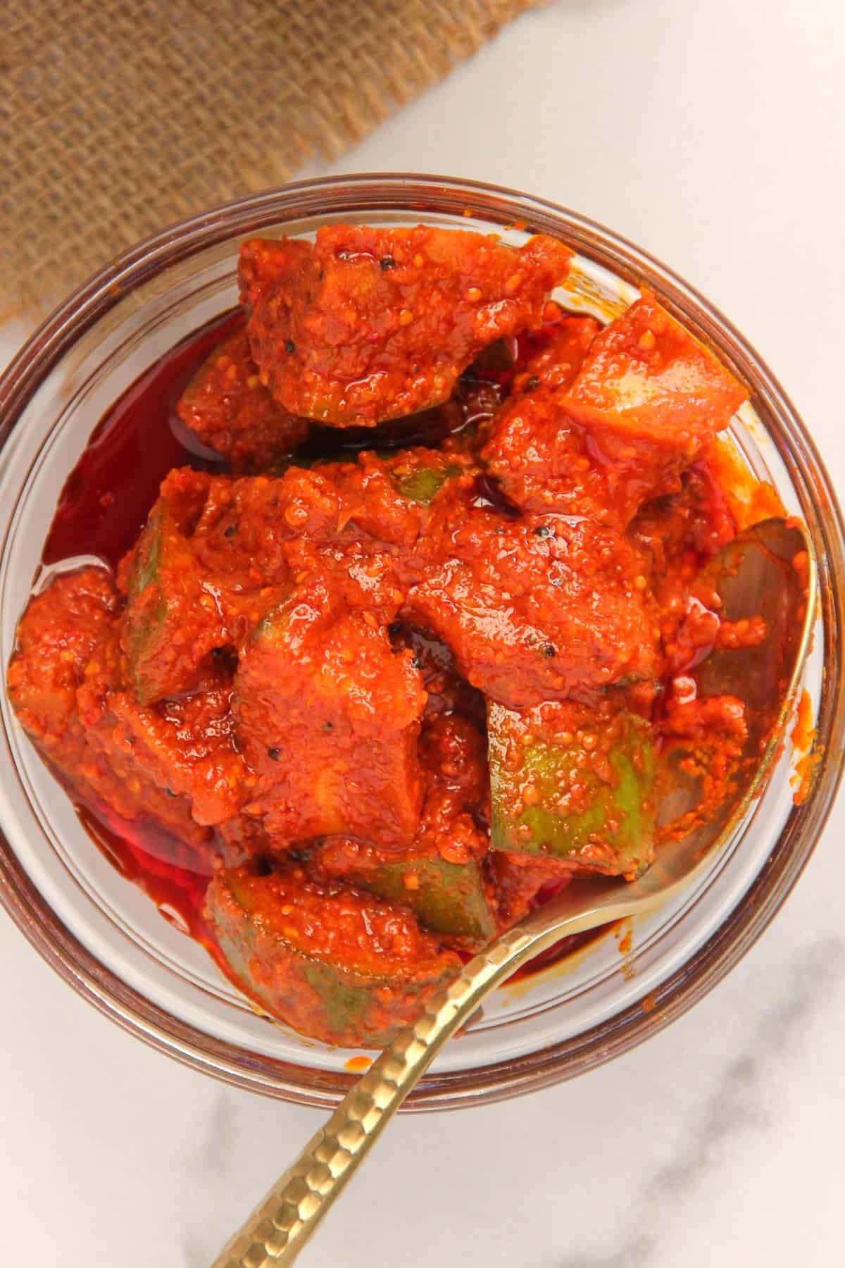 mango pickle in a glass serving bowl with a spoon