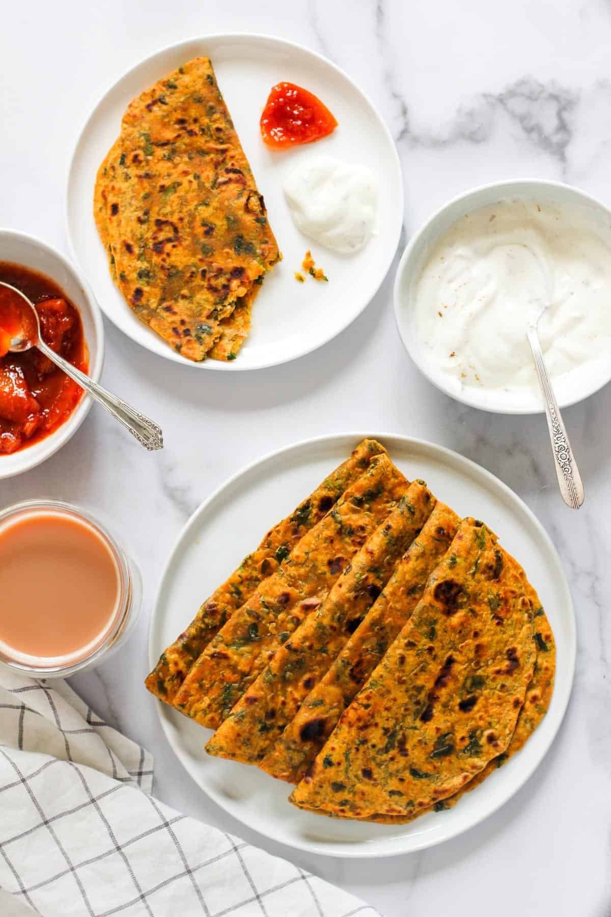 Methi Thepla served in white plates along with yogurt and lemon pickle 