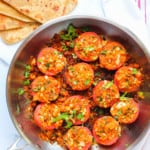 stuffed tomatoes in a frying pan with parathas on the side