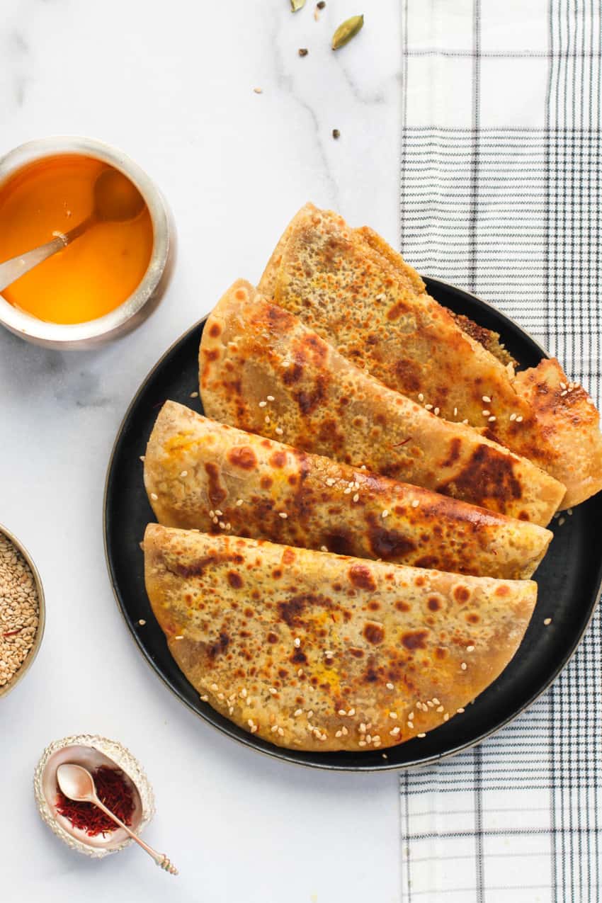 4 sweet sesame parathas in a plate with ghee on the side