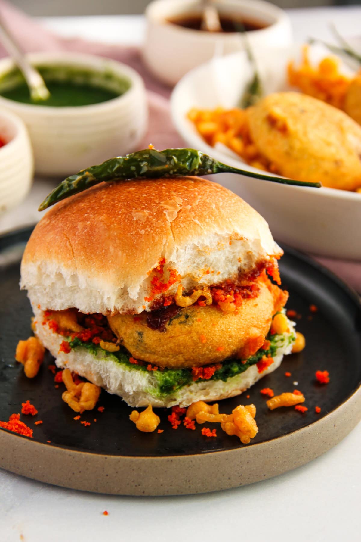 vada pav in a black plate with green fried chili 